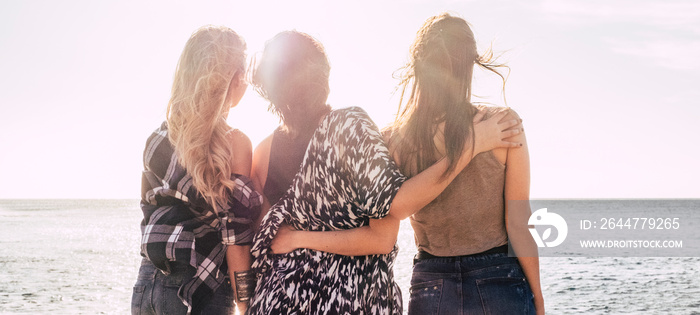 Friendship and together female power concept with three girls friends hug and enjoy the freedom looking at the horizon over the ocean and bright clear sky - love and diversity people