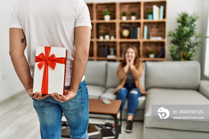 Young couple smiling happy sitting on the sofa surprise with anniversary gift at home.