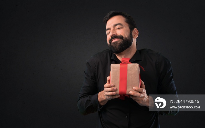 Handsome man with beard holding a gift on black background