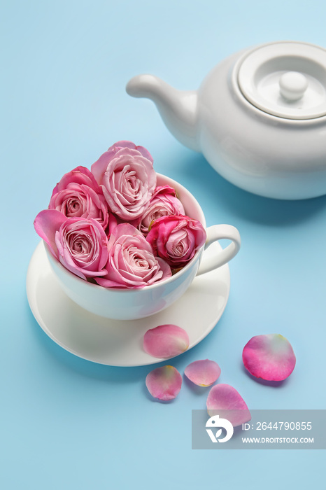 Cup with beautiful pink roses and teapot on color background