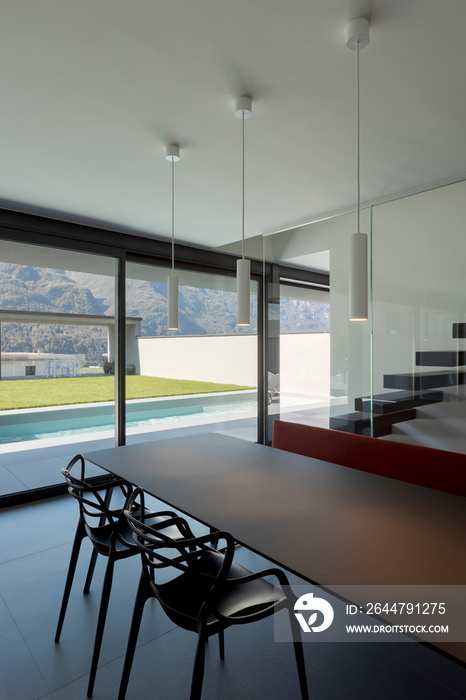 Dining room detail with modern chairs and a red sofa. Outside the window is the pool and green lawn.