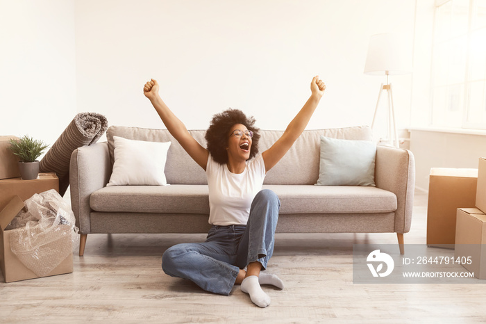 Joyful Black Woman Sitting Among Moving Boxes After Relocation Indoors