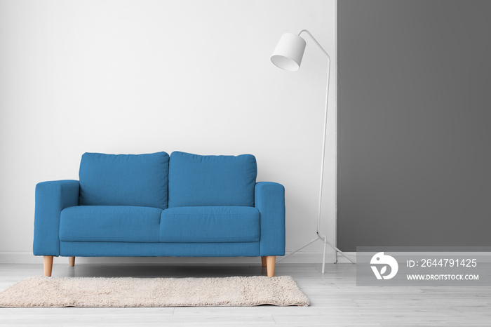 Stylish blue sofa and lamp near light wall