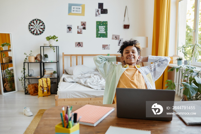 Portrait of mixed-race teenage boy relaxing at home and smiling happily in cozy room interior, copy 