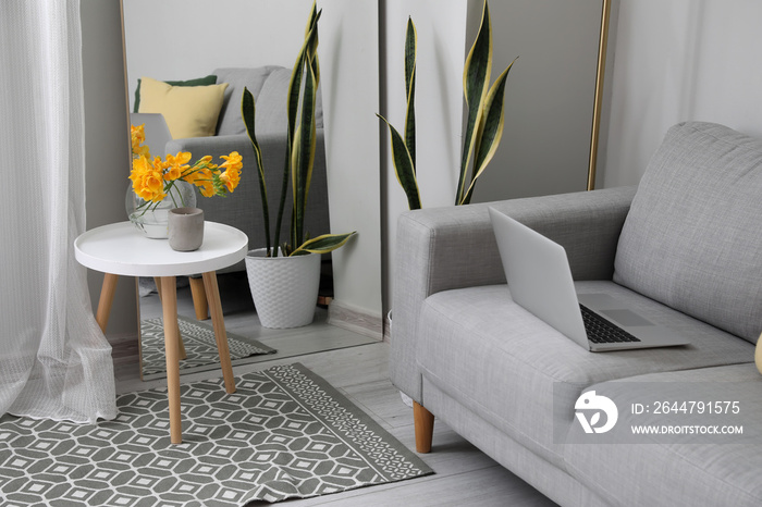 Modern laptop on sofa and vase with flowers on table in living room interior