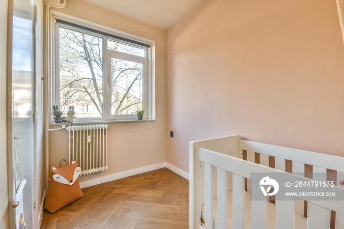 Interior of white room with baby crib and armchair near window with blue chest of drawers in dayligh