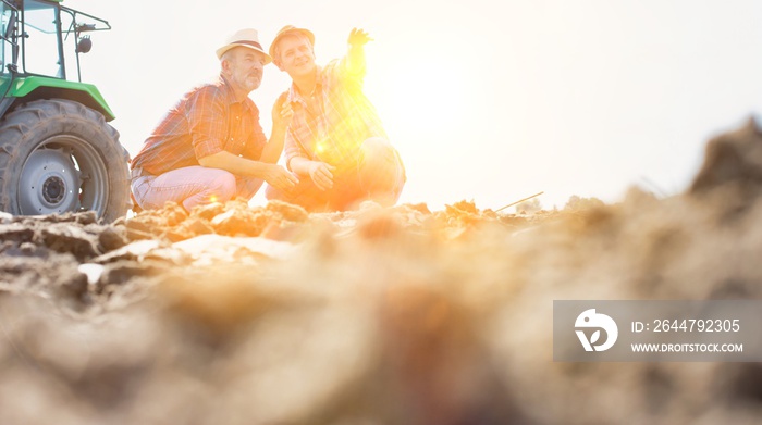 Farmers examining soil in field with yellow lens flare in background