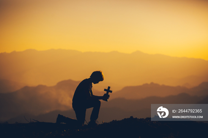 Young man sitting down and praying to God at sunset background. christian silhouette concept.