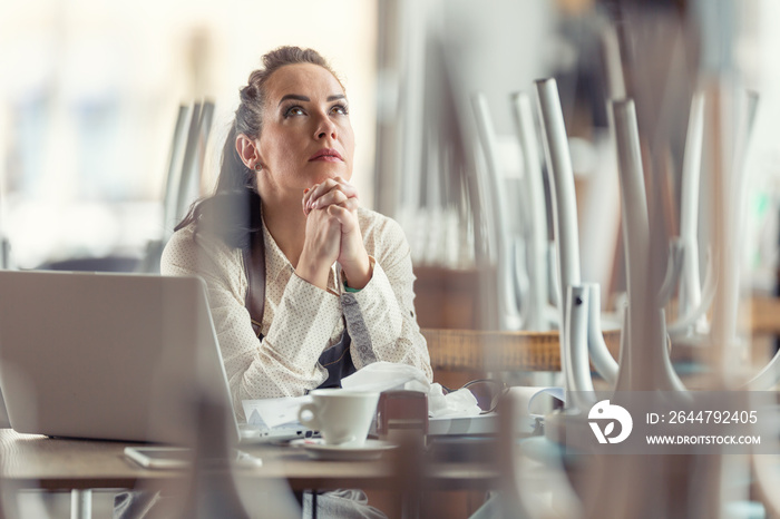 Female business owner prays in a closed  restaurant for better times and the end of coronavirus pand