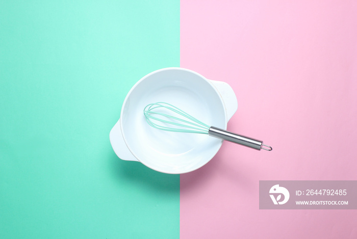 White empty bowl with a whisk on a pastel colored background. Top view, minimalism.