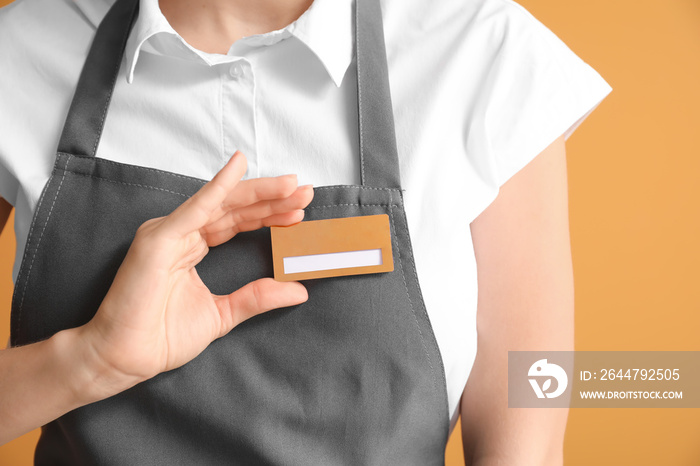 Young female waiter with blank badge on color background