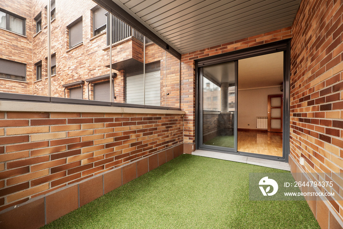 Enclosed terrace with glass and metal, brown bricks and green artificial grass floor in urban reside