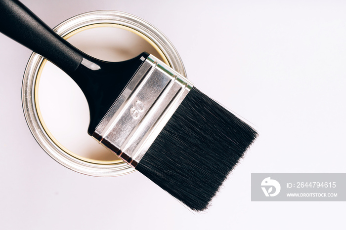 Brush with black handle on open can of white paint on grey background.
