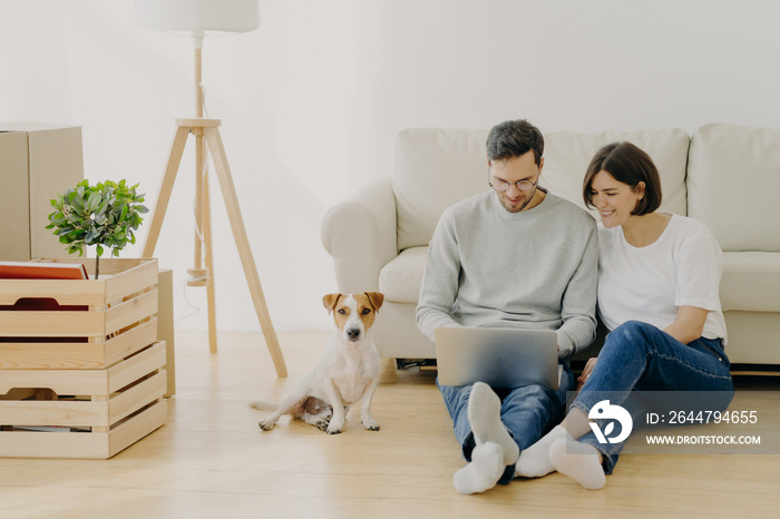 Young European family couple relax during home renovation, focused in laptop computer, plan redecora