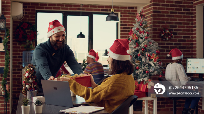 Office employees exchanging presents at work, feeling festive with santa hats in office with christm