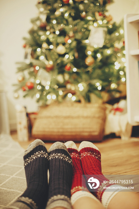 family legs in stylish festive socks on background of golden beautiful christmas tree with lights in