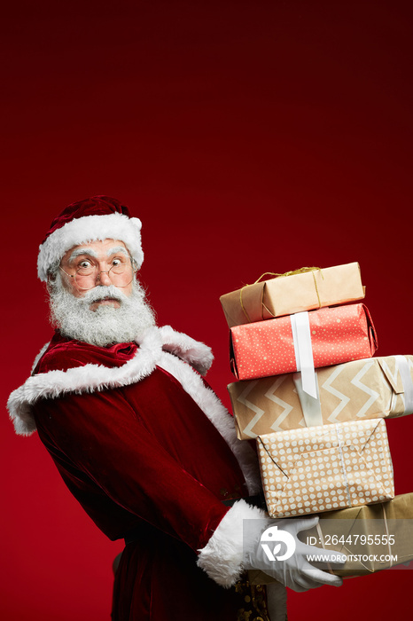 Waist up portrait of fairytale Santa holding stack of Christmas presents over red background, copy s