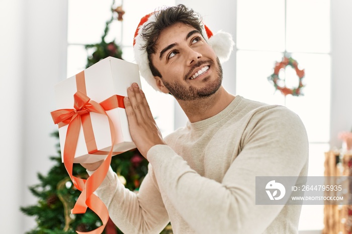 Young hispanic man smiling happy holding gift at home.