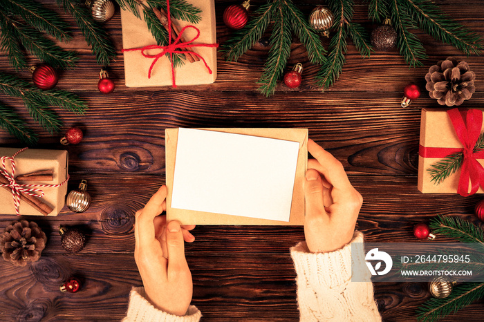 Female hands writing letter to Santa Claus on wooden background with christmas gifts and decoration 