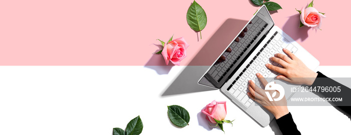 Woman using her laptop with pink roses - flat lay