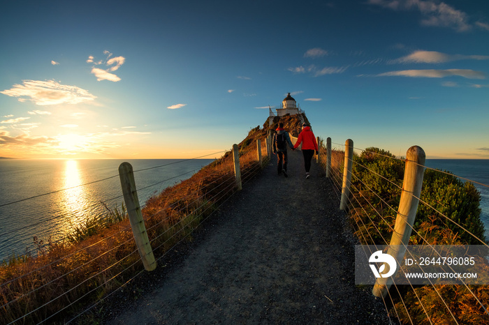 Romantic couple walking towards lighthouse at Nugget Point, Dunedin, New Zealand. Young lovely coupl