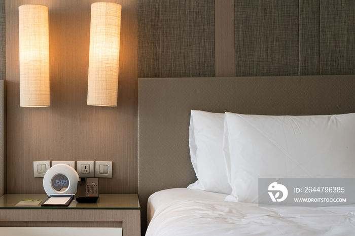 Close up fragment of bedroom with reading lamp and digital alarm clock in modern home or hotel.
