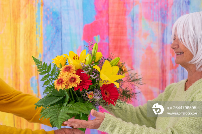 Smiling elderly woman receives flowers as present for anniversary of Valentine day. Colorful backgro