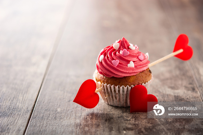 Cupcake decorated with sugar hearts and a cupid arrow for Valentines Day on wooden table