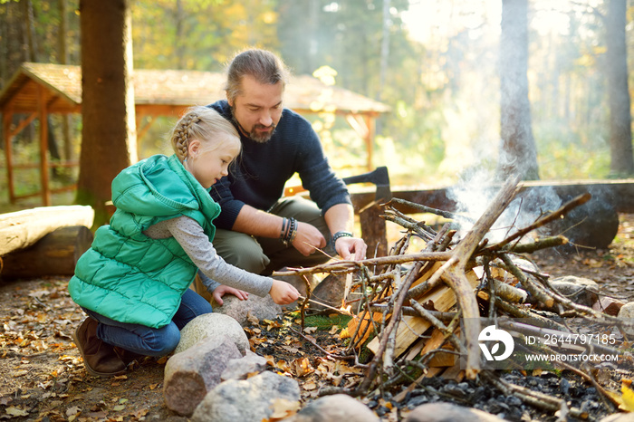 Cute young girl learning to start a bonfire. Father teaching her daughter to make a fire. Child havi