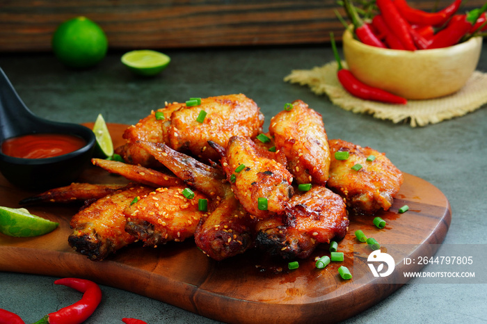 Spicy marinated chicken wings, crispy grilled and chili sauce on a wooden cutting board