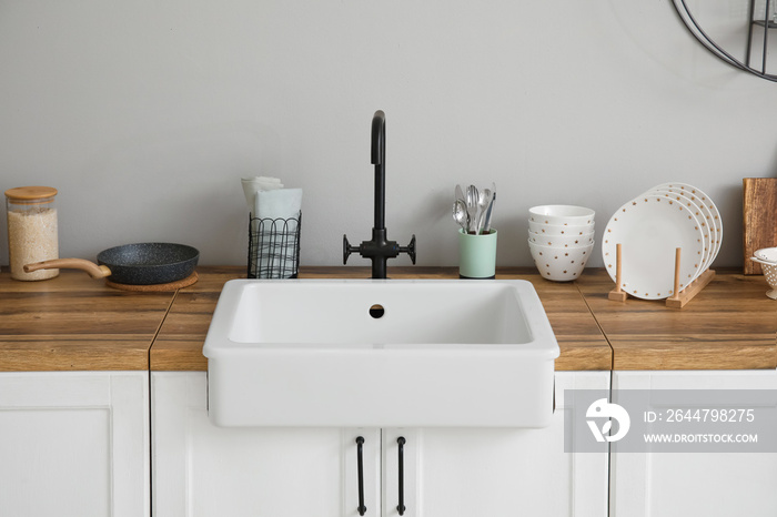 Counters with ceramic sink, kitchen utensils and food near light wall