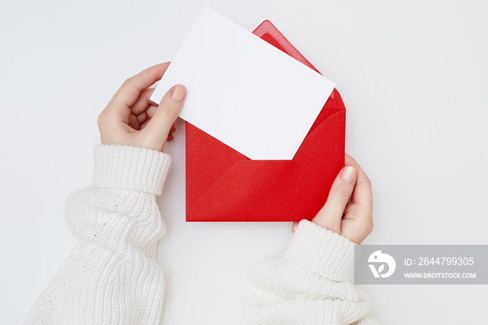 Womens hands holding an empty postcard and red envelope on the white background. Christmas concept