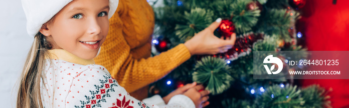 website header of happy girl looking at camera while decorating christmas tree with family