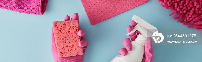 panoramic shot of housekeeper in pink rubber gloves holding sponge and spray bottle on blue with rag