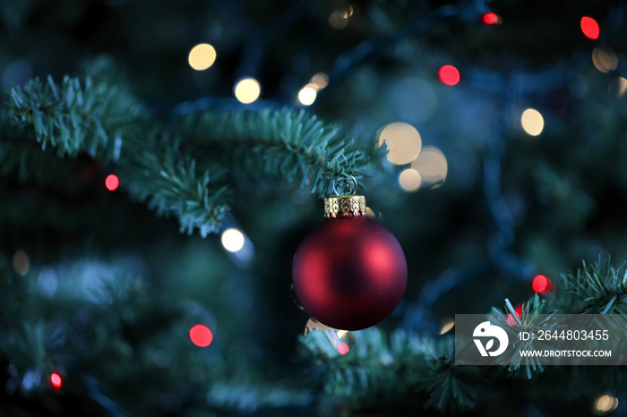 Traditional artificial Christmas tree with red ball ornament and glowing lights in background