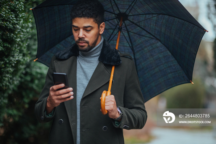 Businessman with umbrella texting to client on smartphone