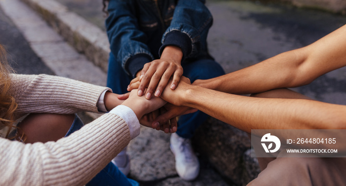 Group of friends sitting together stacking their hands on one an