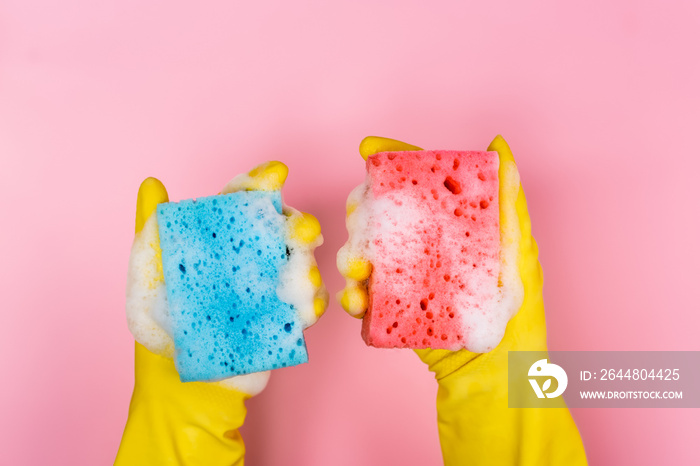 Top view of hands in rubber gloves holding sponges with soap foam on pink background