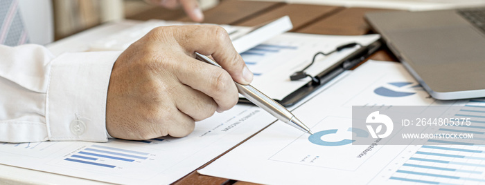 A close-up view of a businessman holding a pen pointing at a bar chart on a corporate finance docume