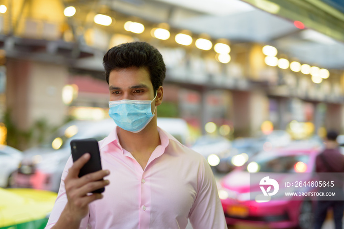 Young Indian businessman with mask using phone in the city streets