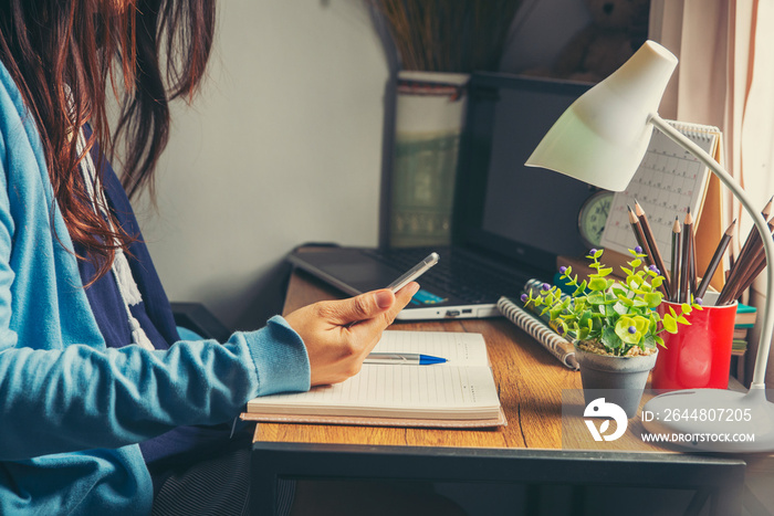 Study and technology concept.Person side view of sad woman holding smartphone and reading book.Asian