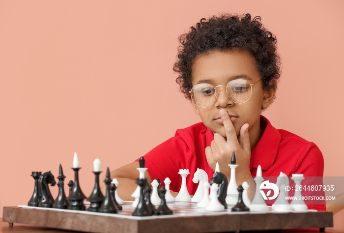 Cute African-American boy playing chess on color background