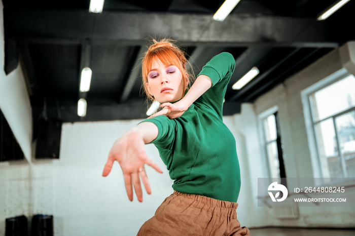 Red-haired professional choreographer in a green turtleneck stretching her arm