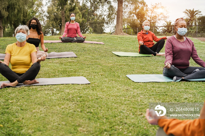 People doing yoga class outdoor sitting on grass while wearing safesty masks during coronavirus outb