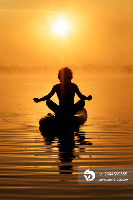 Silhouette of relaxed man sitting in lotus pose on sup board