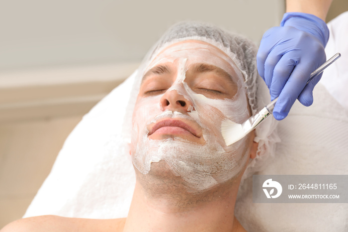 Handsome man undergoing treatment with facial mask in beauty salon