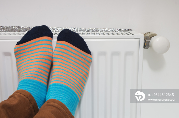 Female feet in bright socks against the background of a house heater. Conceptual image of home heati