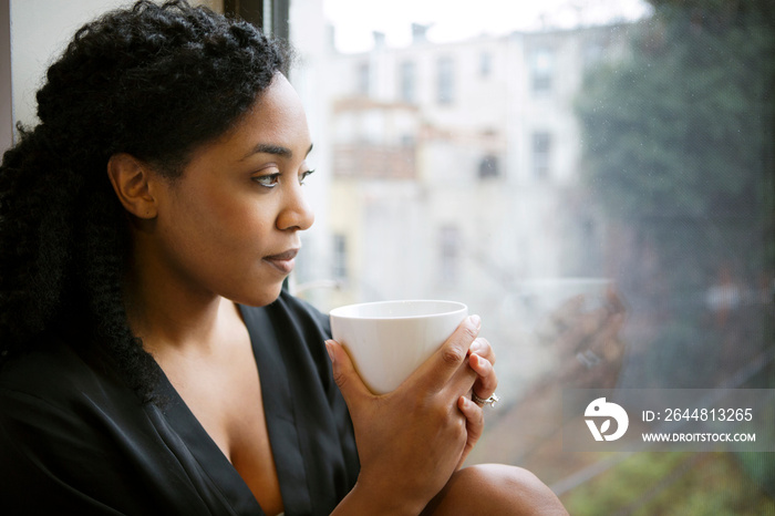 Woman looking through window holding coffee cup