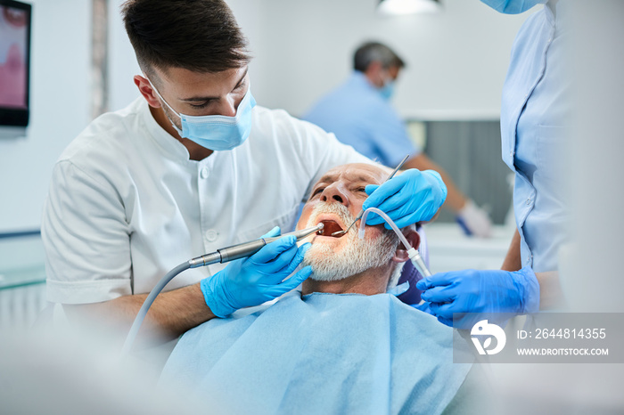 Senior man having teeth polish procedure during appointment with dentist at clinic.