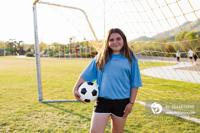 Portrait of smiling girl holding soccer ball standing on grassy field against net